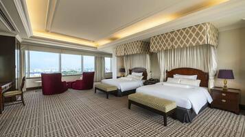 Ein Hotelzimmer mit zwei Betten, einem roten Sessel, einem großen Fenster mit Blick auf die Stadt und einem gemusterten Teppich.