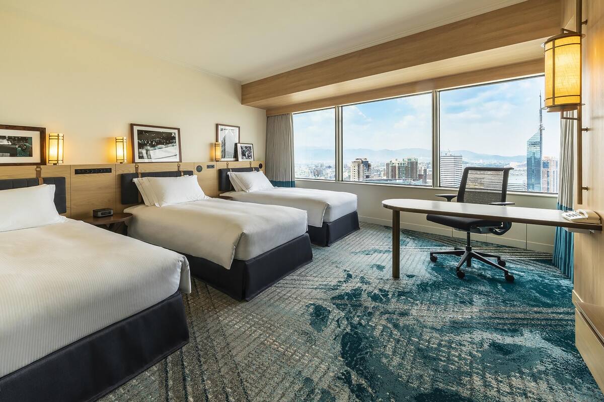 Une chambre d’hôtel avec deux lits, un bureau et une grande fenêtre donnant sur la ville.
