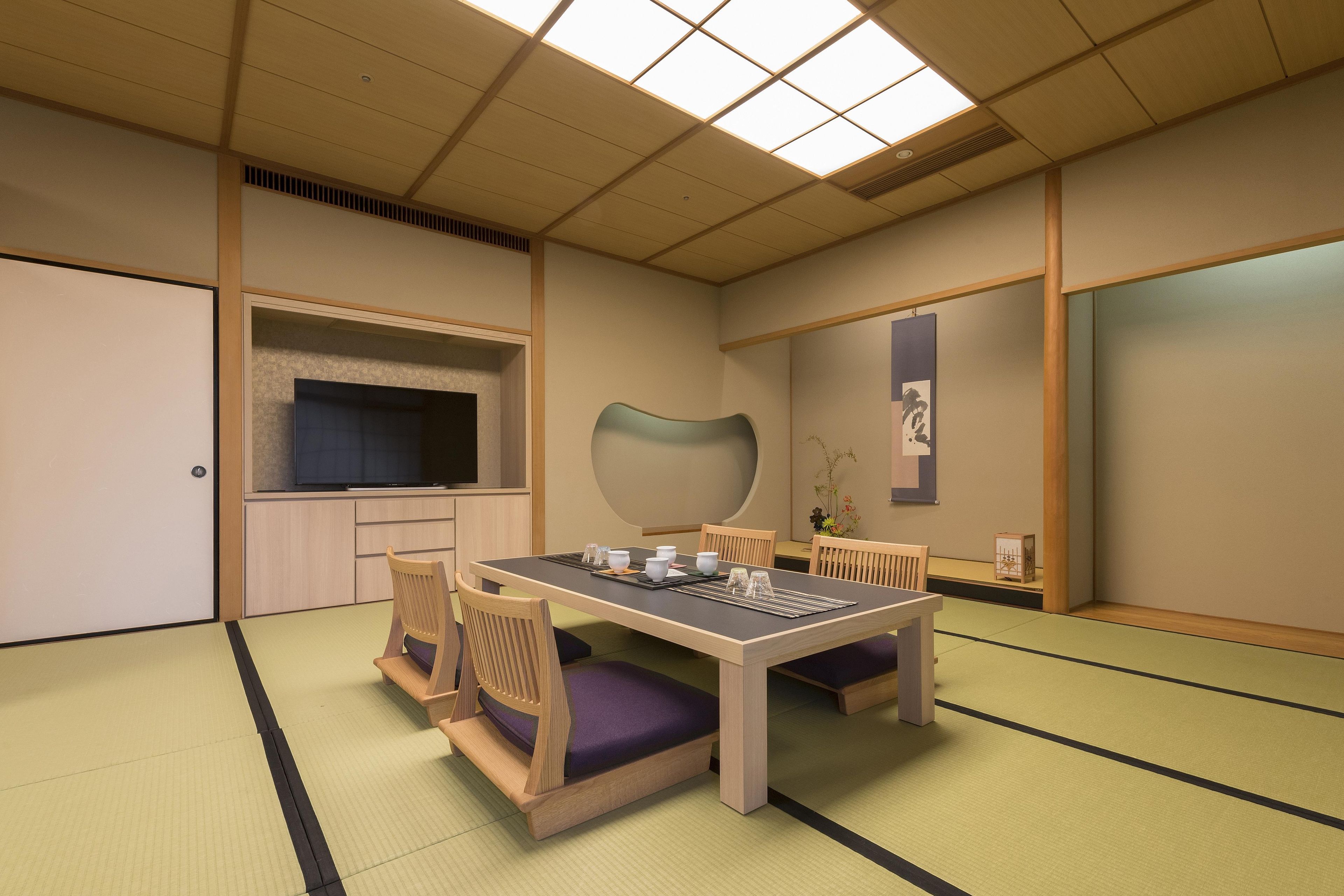 A traditional Japanese-style room with tatami flooring, a low table with cushions, and a television mounted on the wall.