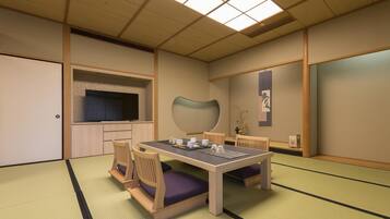 A traditional Japanese-style room with tatami flooring, a low table with cushions, and a television mounted on the wall.