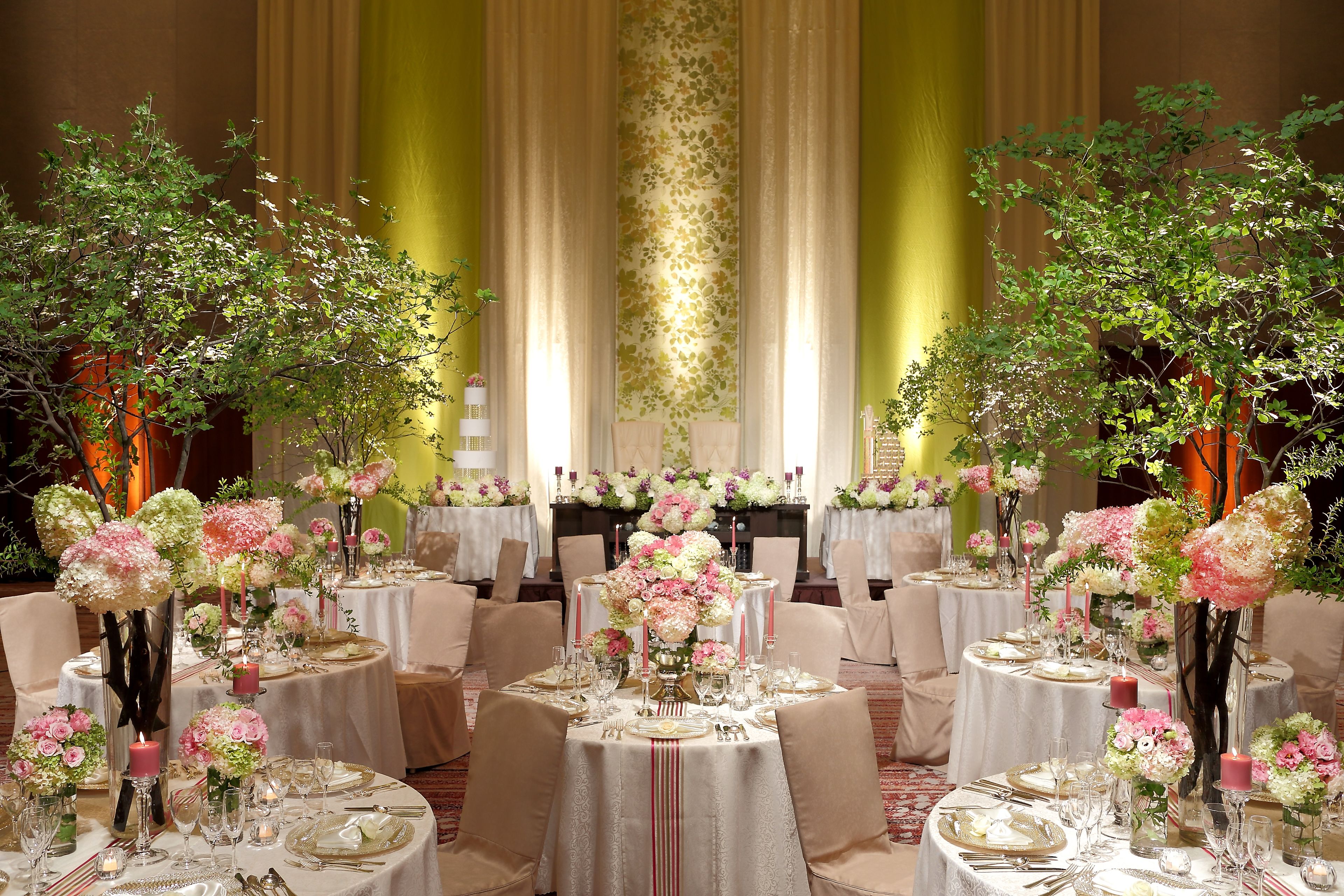 A banquet hall with round tables set for a formal event, adorned with floral centerpieces and candles.