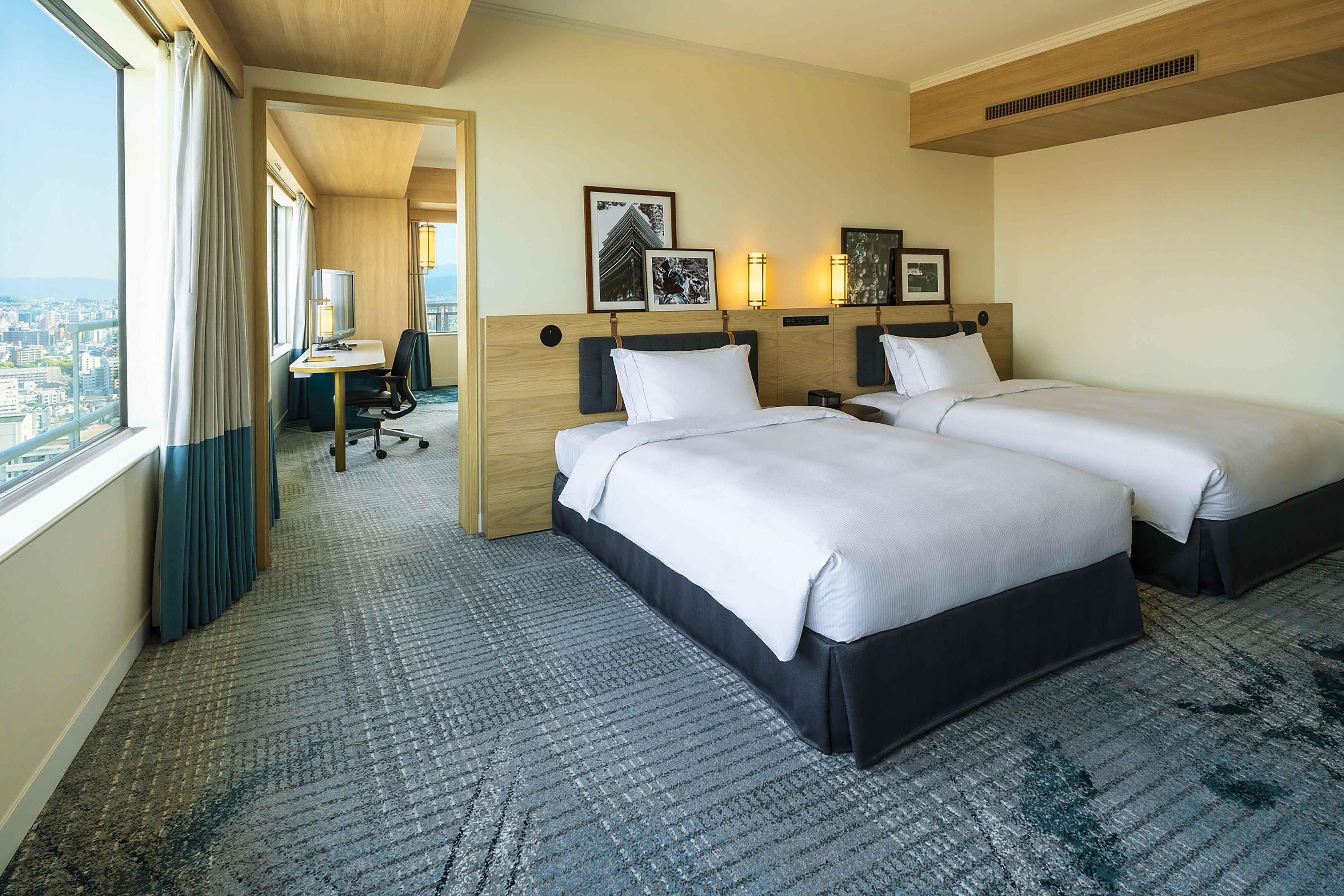 Une chambre d’hôtel avec deux lits, un bureau et une vue sur la ville.