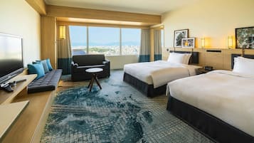A hotel room with a large bed, a smaller bed, a sofa, a TV, and a view of a cityscape.