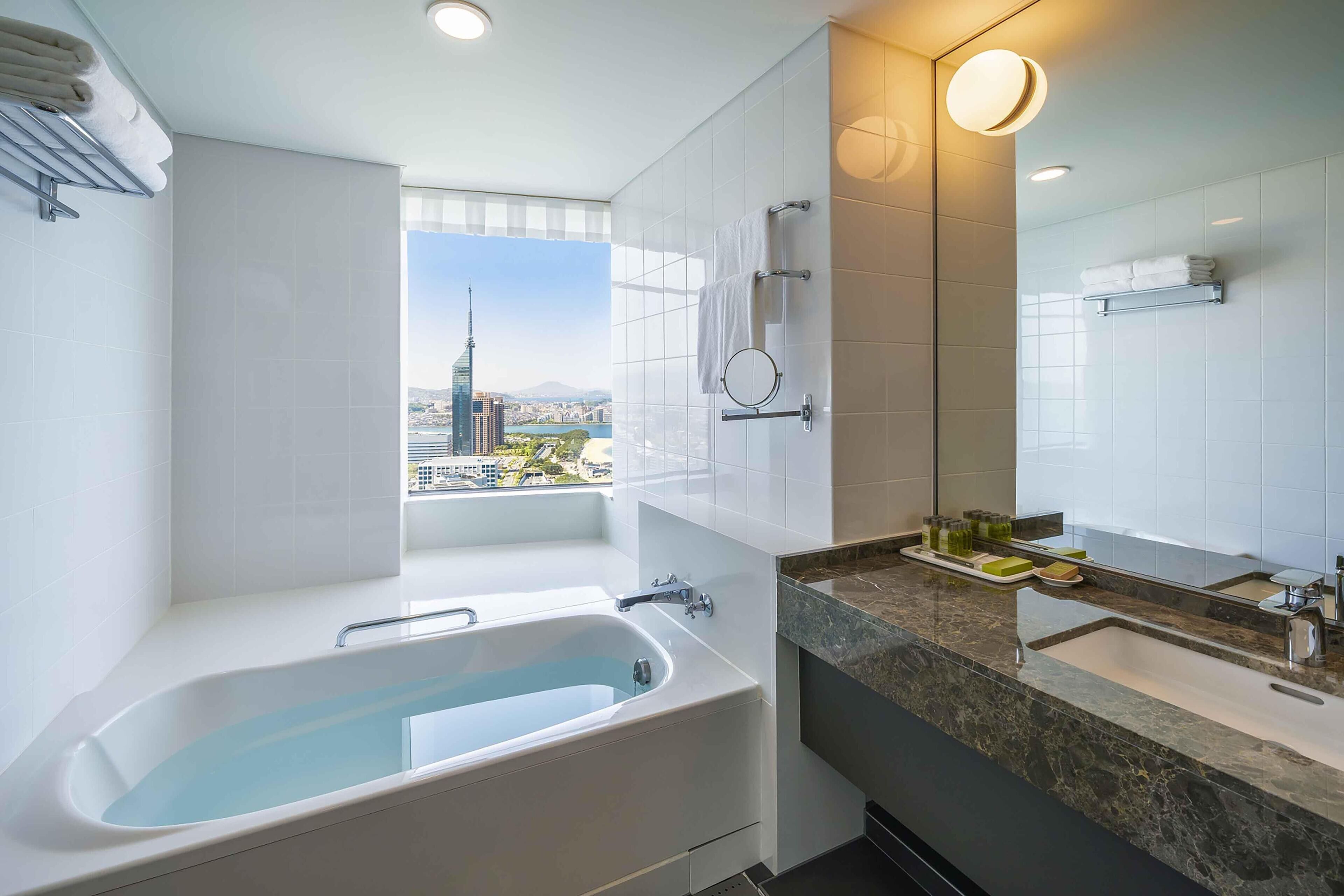 A modern bathroom with a bathtub, a large mirror, and a view of a cityscape.