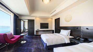 A hotel room with a bed, a TV, a desk, a chair, and a view of the sea.