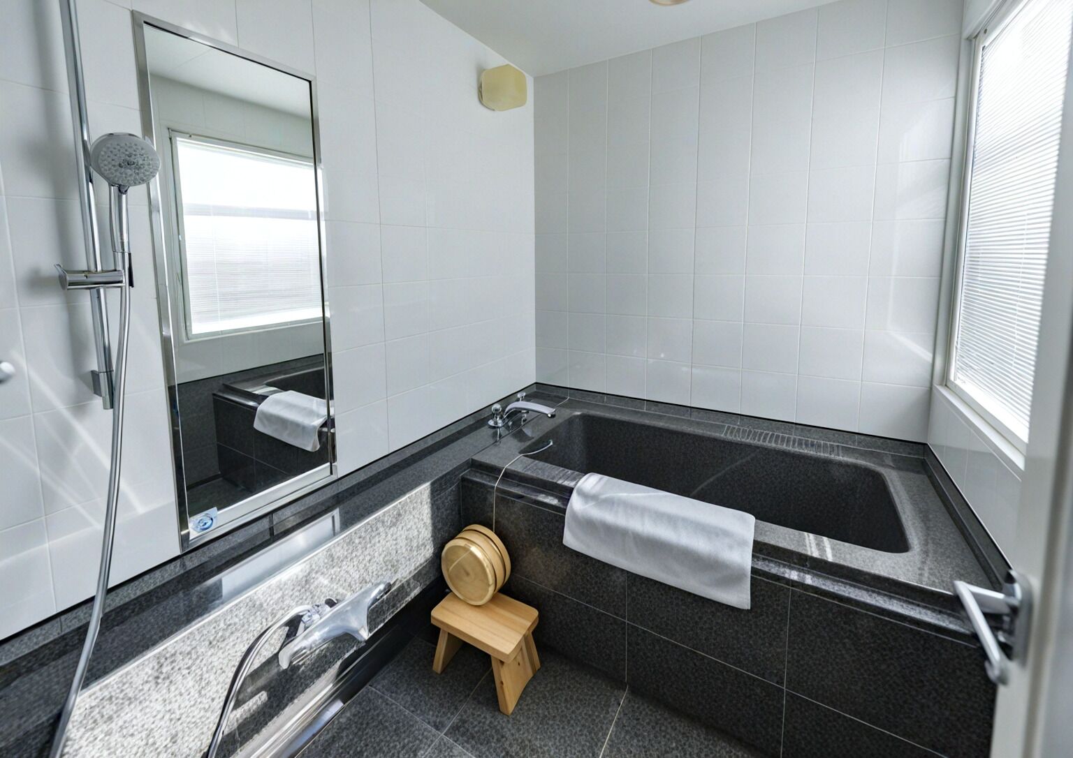 Une salle de bain moderne avec une grande baignoire, une douche, un lavabo et un petit tabouret en bois.