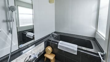 A modern bathroom with a large bathtub, a shower, a sink, and a small wooden stool.