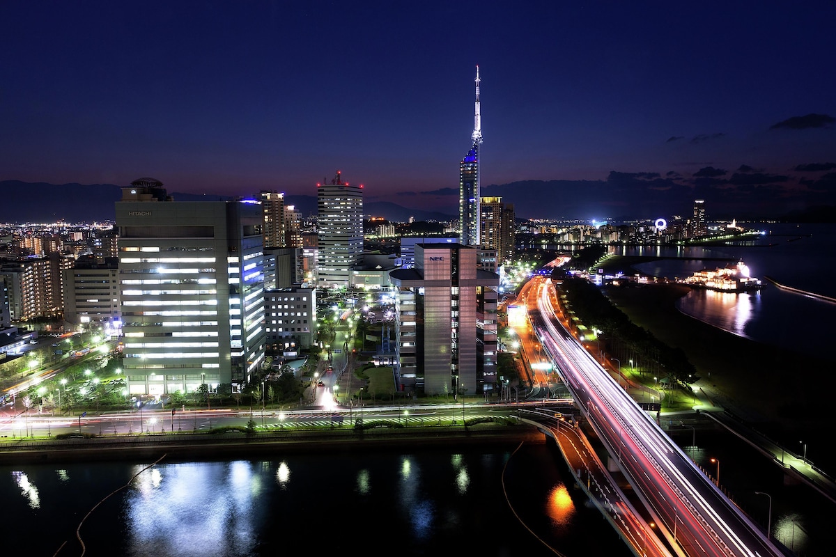 A cityscape at night with illuminated buildings, a river, and a bridge.