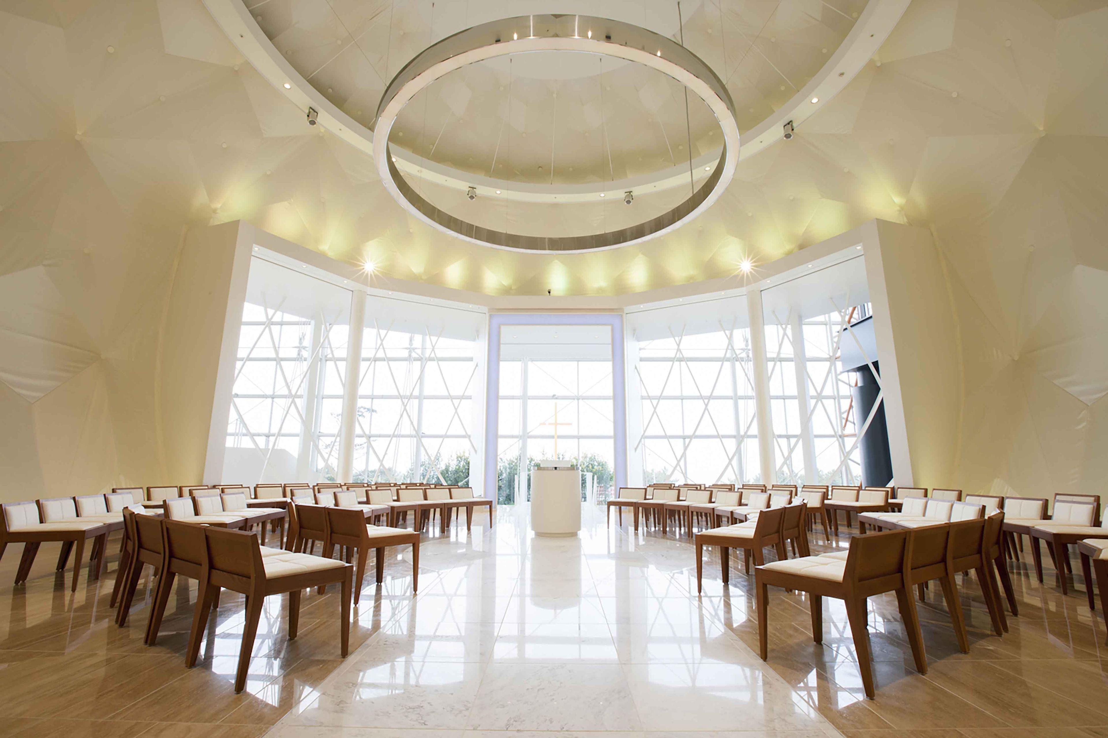 A spacious hall with a high ceiling, large windows, and a central aisle leading to an altar.