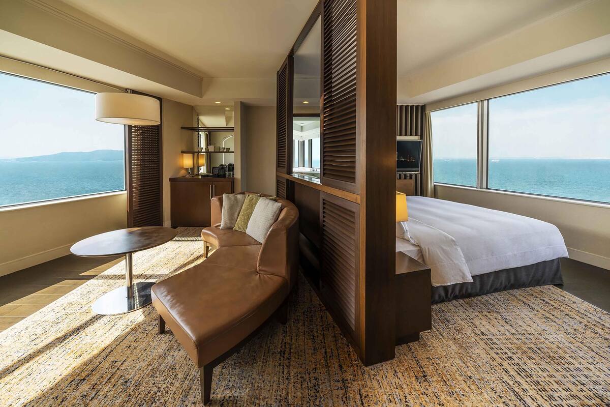Une chambre d’hôtel avec un lit, un canapé, une petite table, une lampe, un miroir et une vue sur la mer.
