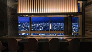 Un bar con vista a la ciudad de noche, un ventanal grande y una decoración interior moderna.