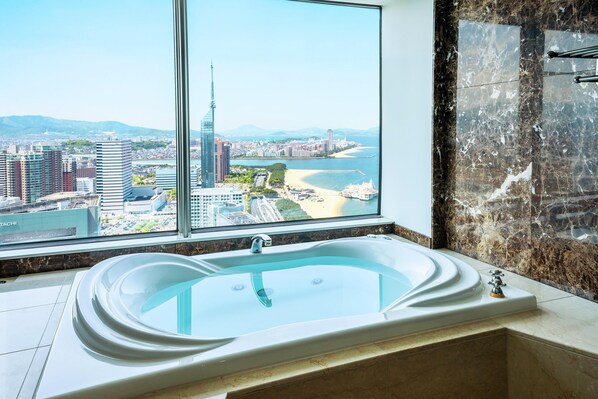 A modern bathroom with a large bathtub, a view of a cityscape through a large window, and a marble wall.