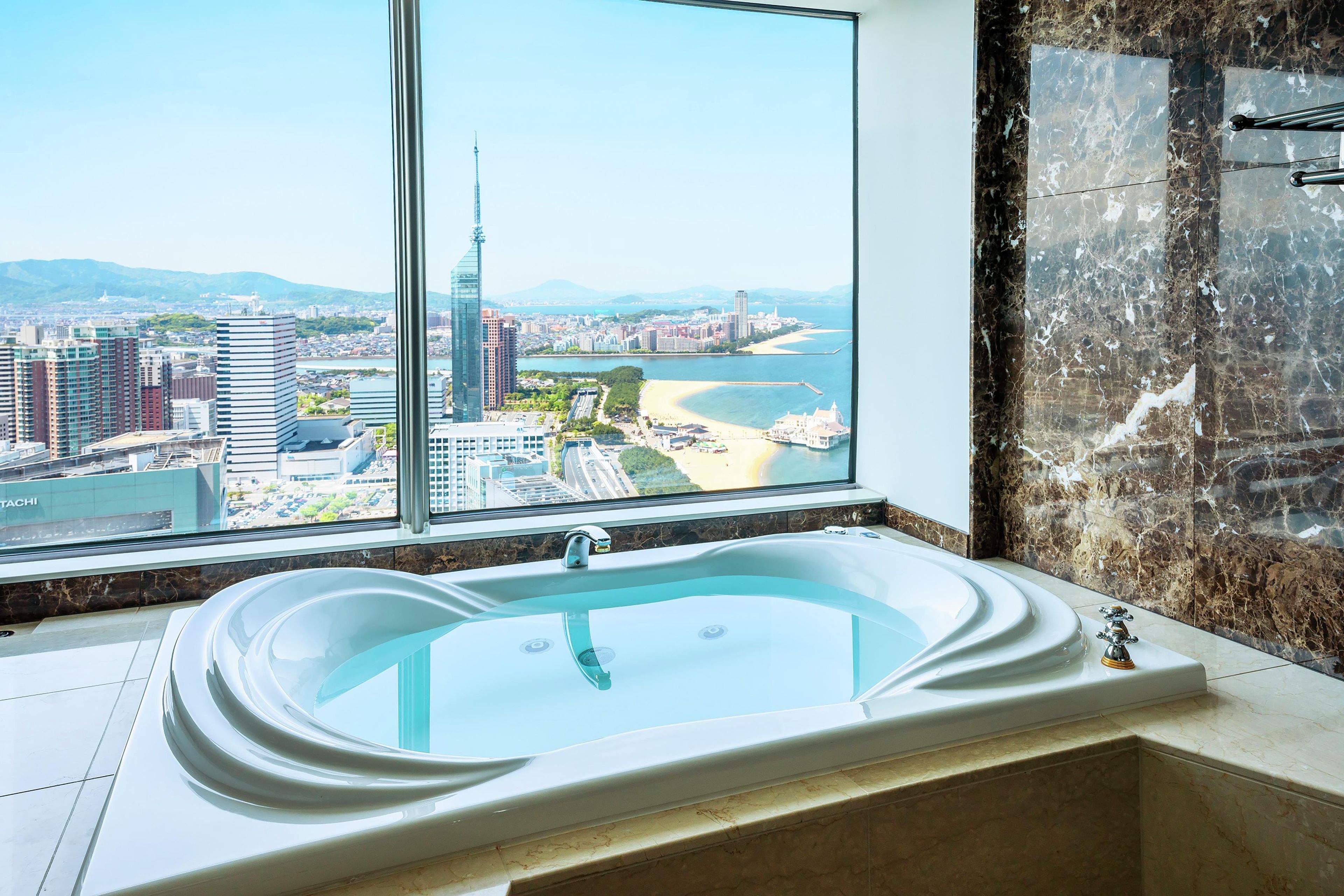 A modern bathroom with a large bathtub, a view of a cityscape through a large window, and a marble wall.