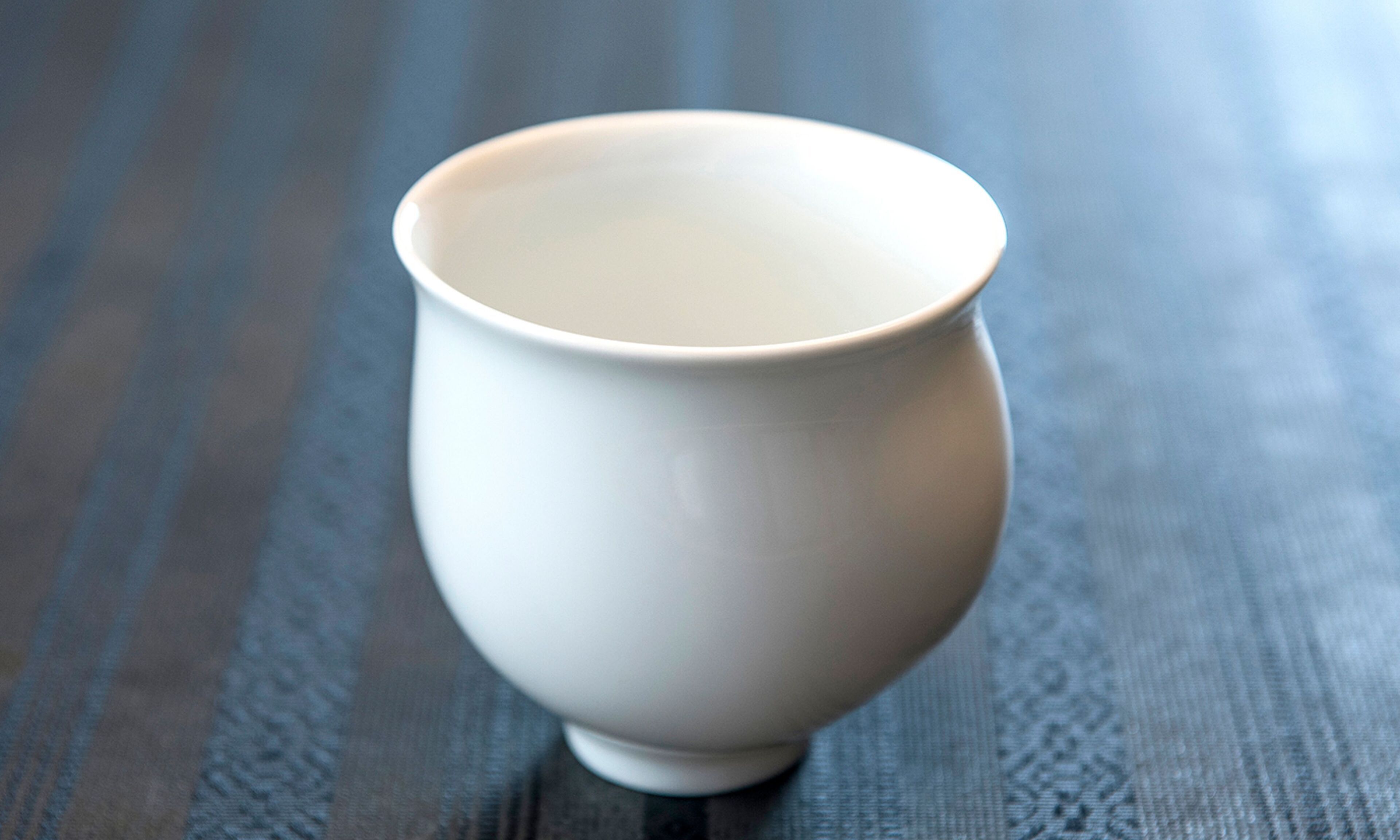 A white ceramic cup on a textured wooden surface.