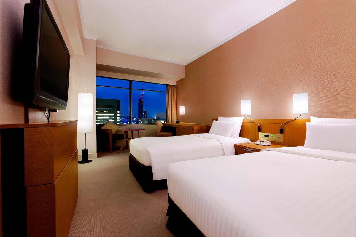Une chambre d’hôtel avec deux lits, une télévision, un bureau, une chaise et une vue sur le paysage urbain de nuit.