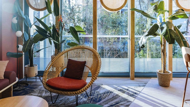 Una habitación con ventanas amplias, una silla de mimbre, un sofá y plantas en macetas.