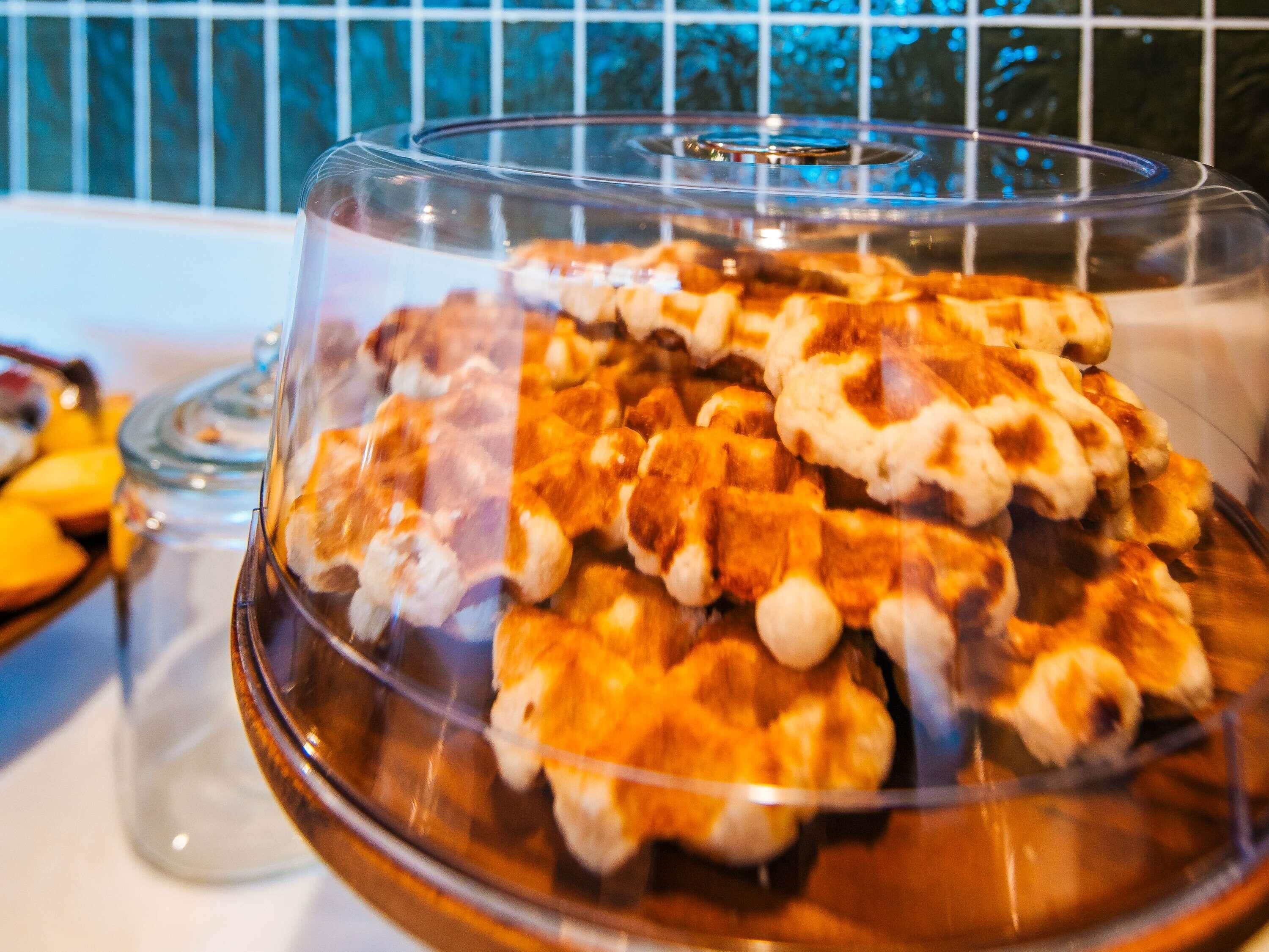 A buffet with a variety of food items, including waffles and other desserts, served in a glass-covered dish.