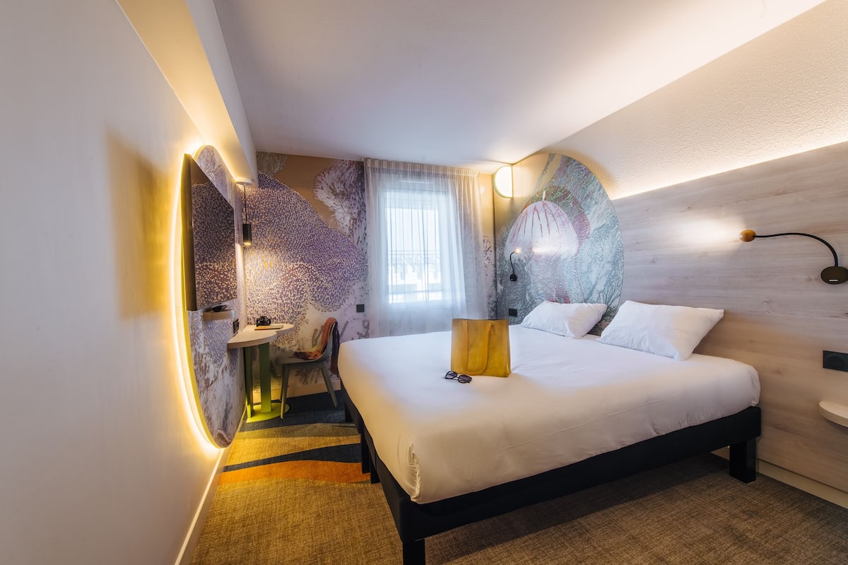 A modern hotel room with a large bed, a desk, and a chair.