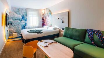 Una habitación de hotel moderna con una cama, un sofá verde, una mesa de madera y una silla.