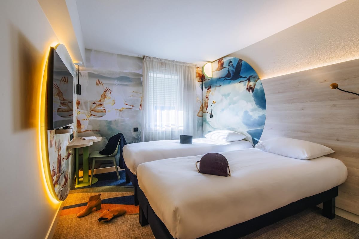 A hotel room with a bed, a desk, a chair, and a TV.