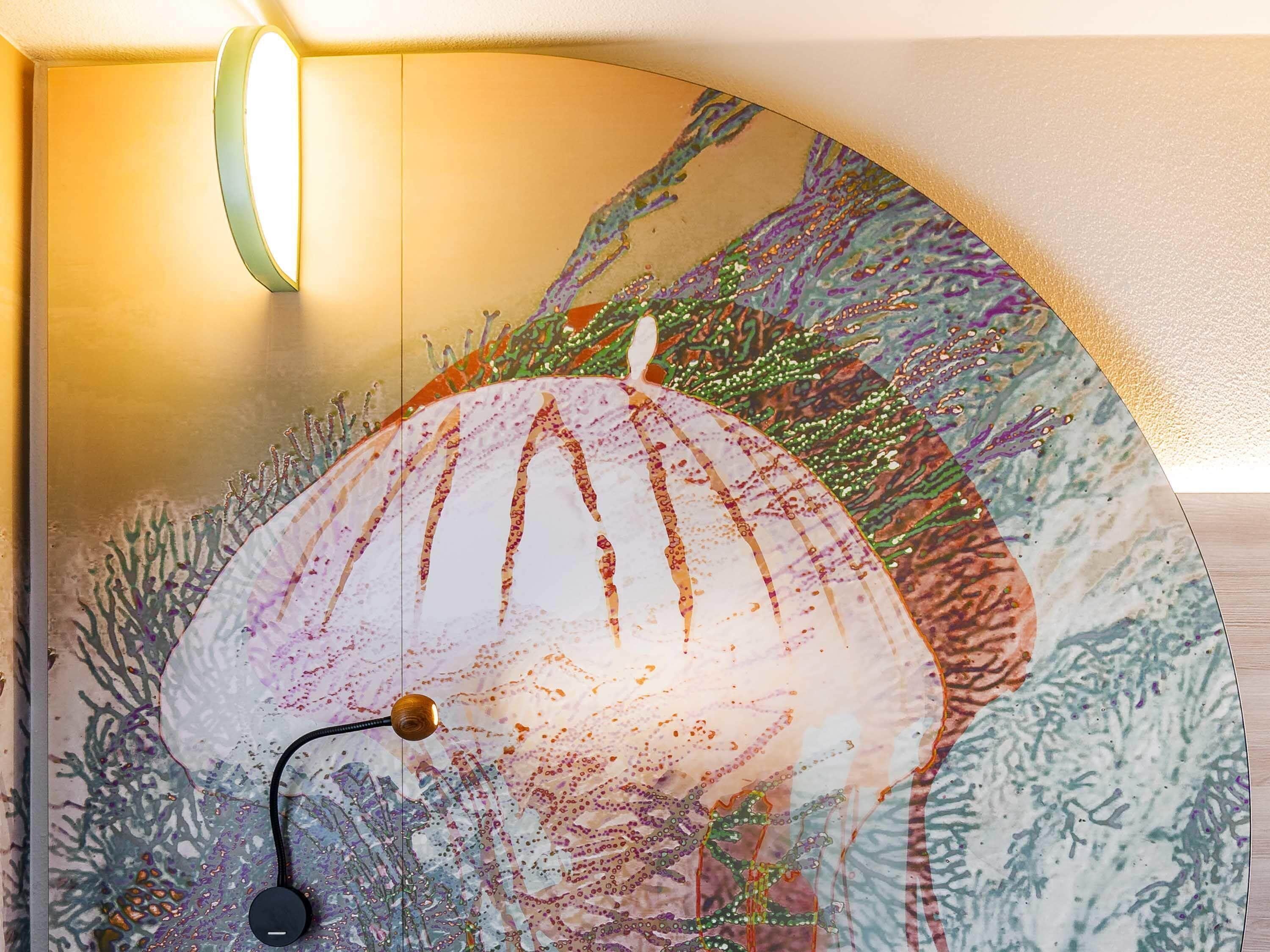 A wall with a large, colorful mural of marine life, a round mirror, and a light fixture.