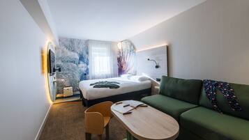 A hotel room with a bed, a green sofa, a wooden table, and a chair.