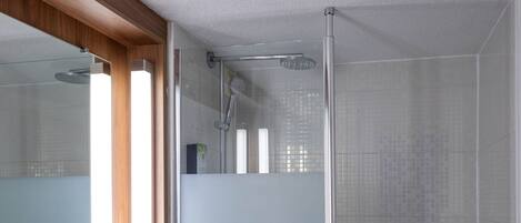 Un baño con lavamanos blanco, cabina de ducha de vidrio y tocador de madera.