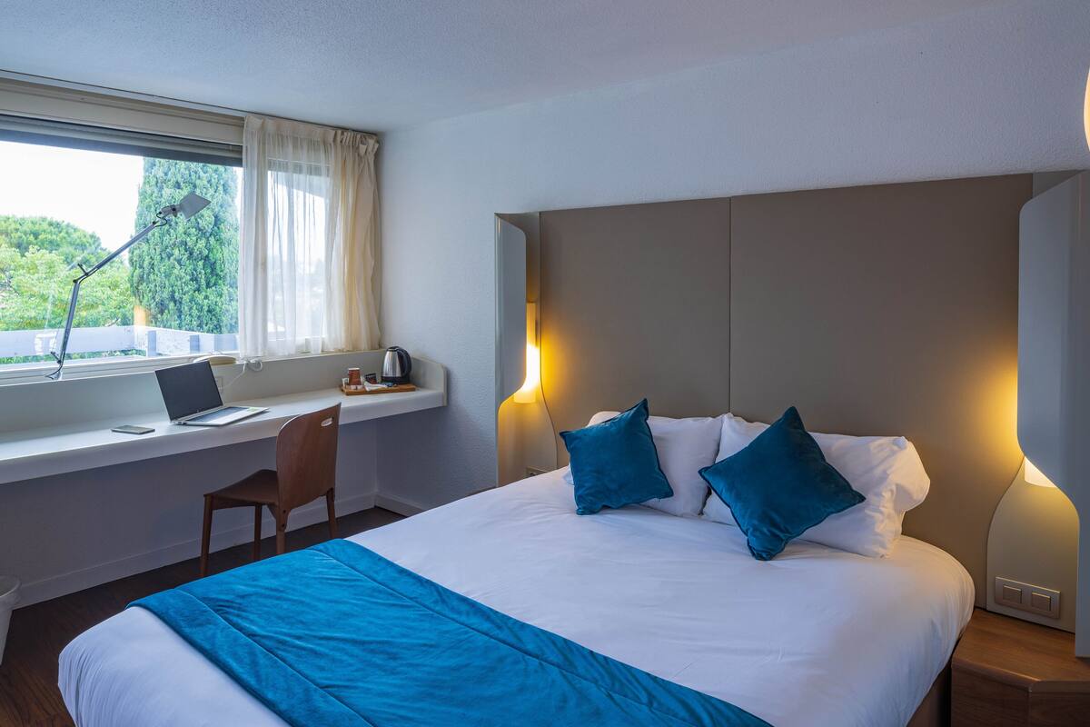A hotel room with a bed, a desk with a laptop, and a chair.