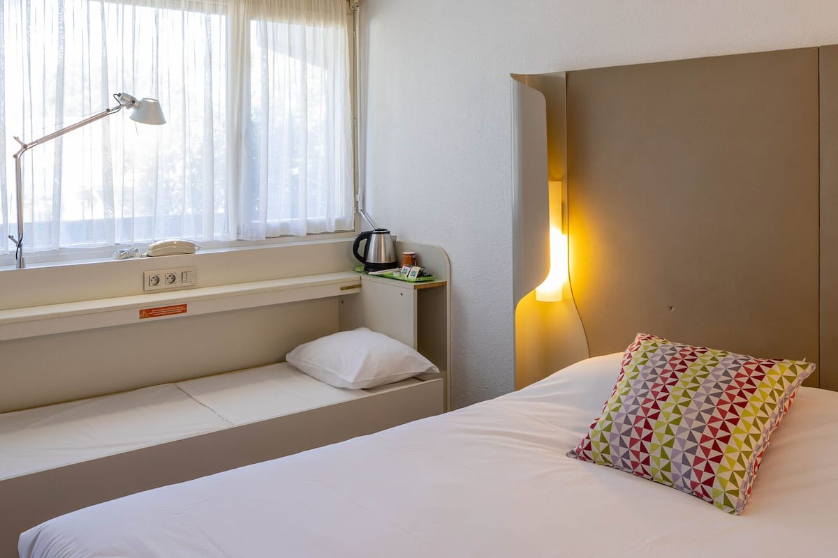 A neatly made bed with a pillow, a hat, and a book titled "Plages Corse" on the bedside table.