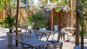 An outdoor patio with wooden tables and chairs, surrounded by potted plants and a wooden fence. - Noemys Arles (Arles)
