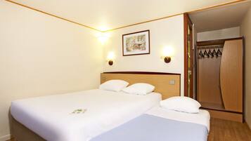 A hotel room with two beds, a wooden headboard, a framed picture on the wall, and a wooden wardrobe.