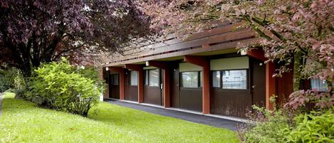 A row of single-story buildings with a covered walkway, surrounded by lush greenery and flowering trees.
