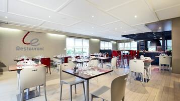 A restaurant with multiple tables and chairs, a kitchen area, and large windows allowing natural light.