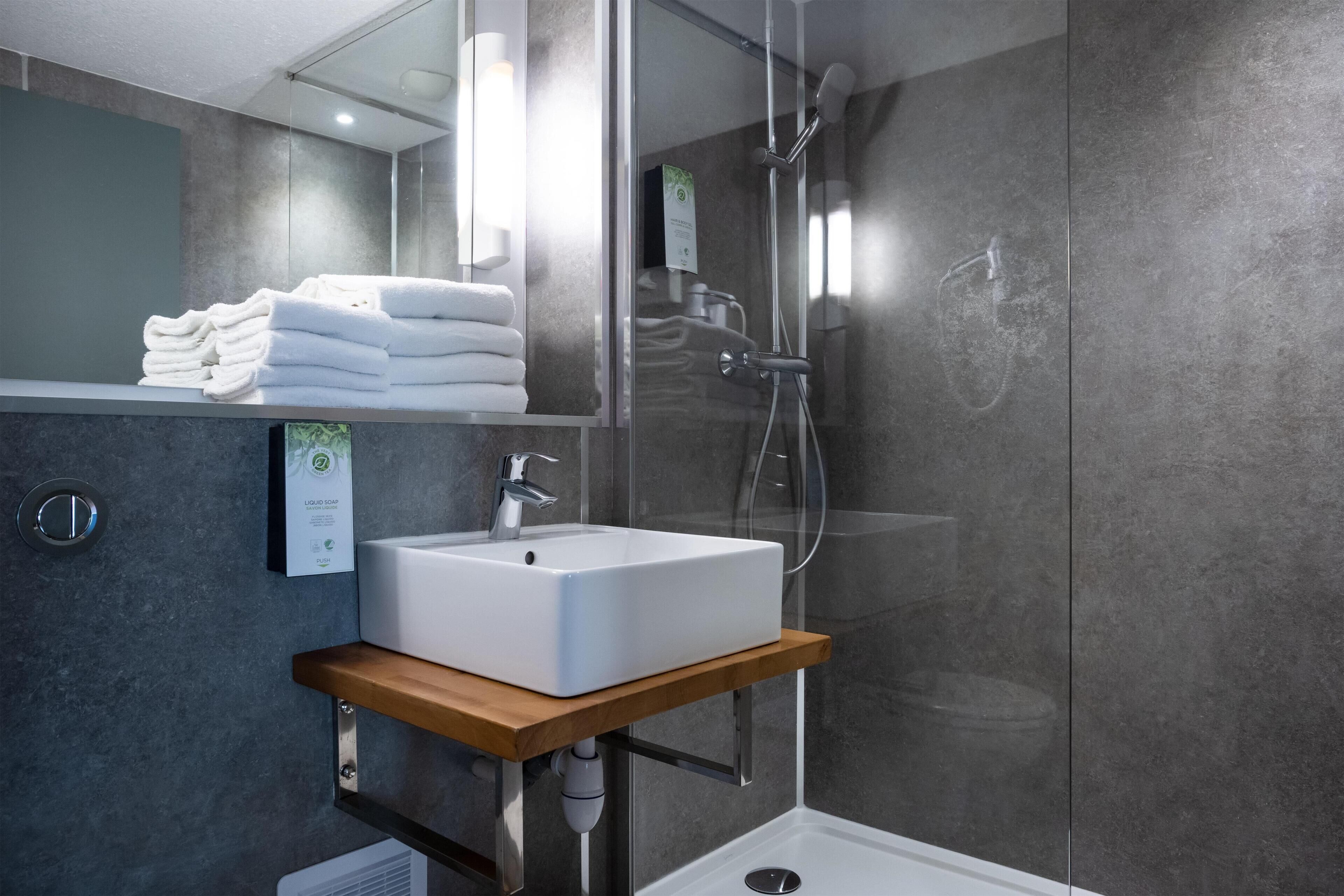 A modern bathroom with a glass-enclosed shower, a white sink on a wooden shelf, and neatly folded towels.