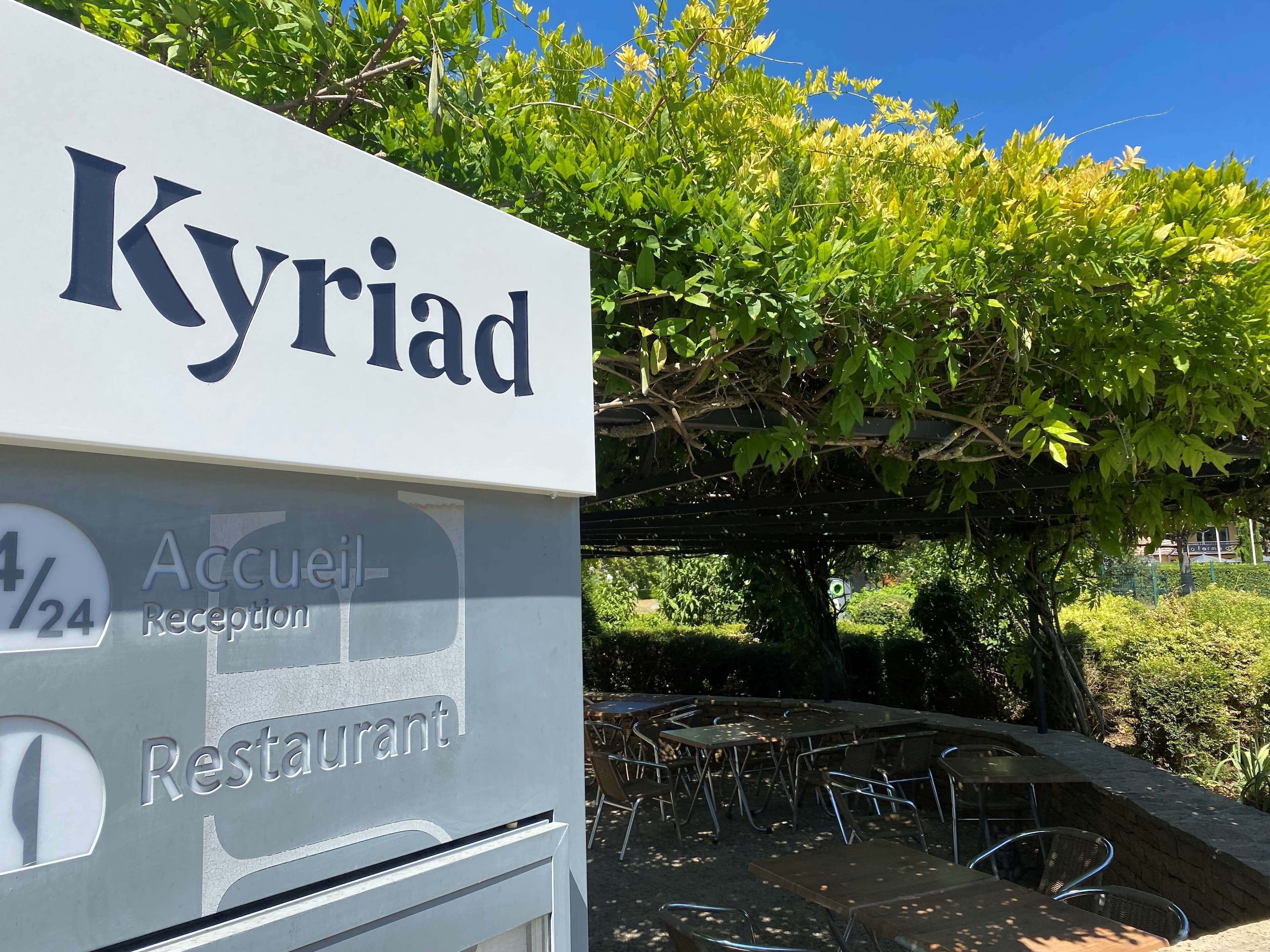 A sign for "Kyriad Restaurant" with a reception area and outdoor seating.
