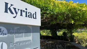 A sign for "Kyriad Restaurant" with a reception area and outdoor seating.