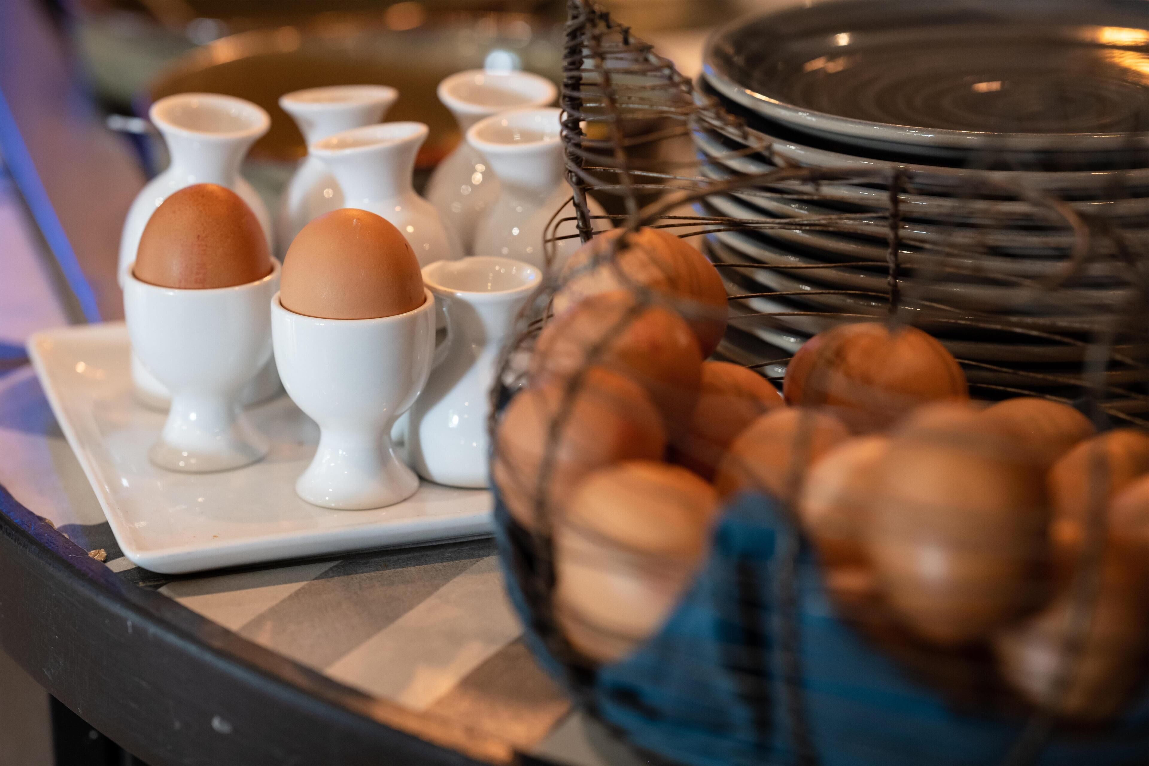 A breakfast buffet with various egg dishes and a wicker basket filled with eggs.