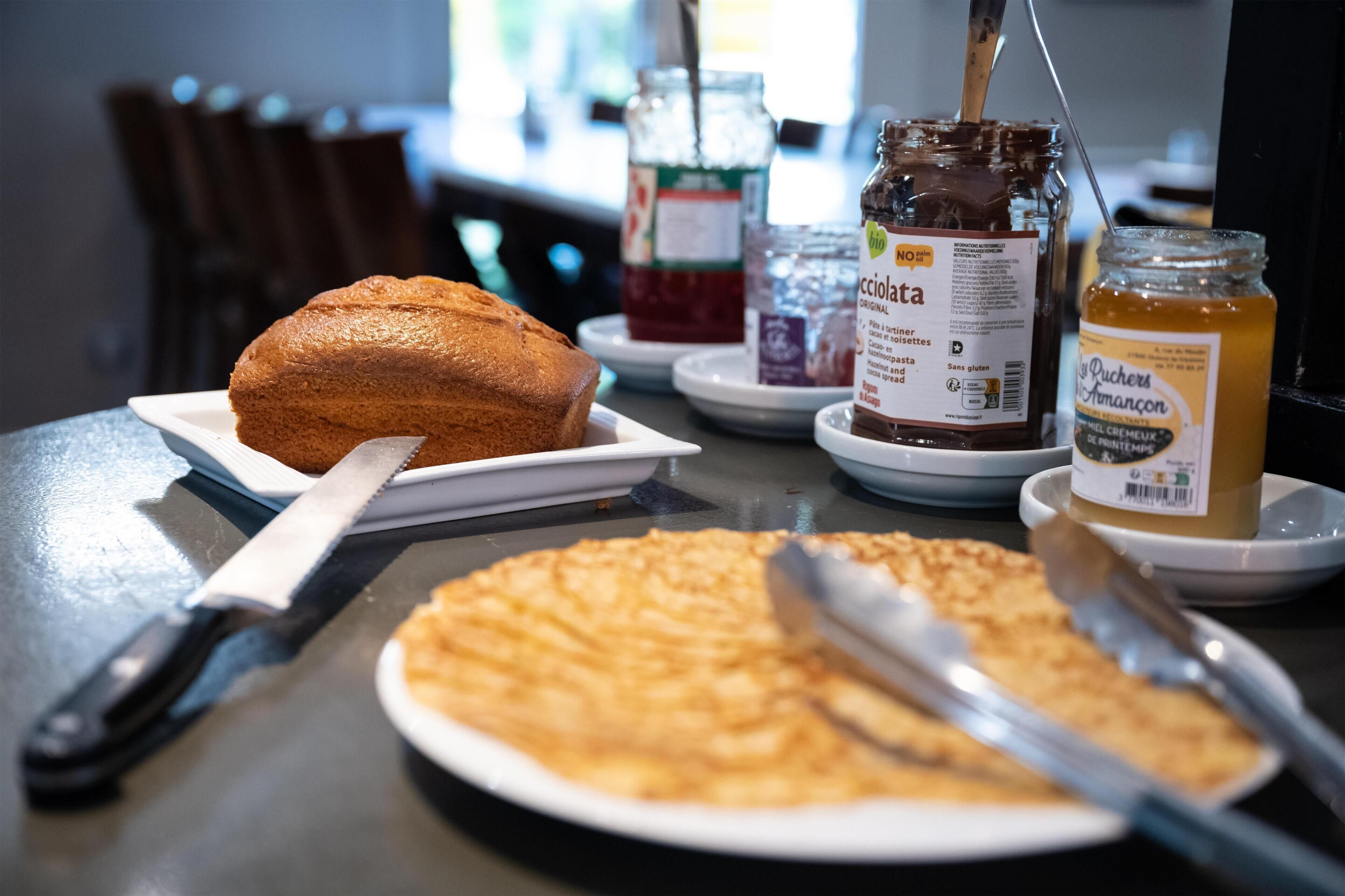 A table with a loaf of bread, a plate of croissants, and jars of spreads.