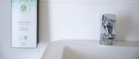 Un baño con un lavamanos blanco, un grifo cromado y una caja de jabón de té verde.