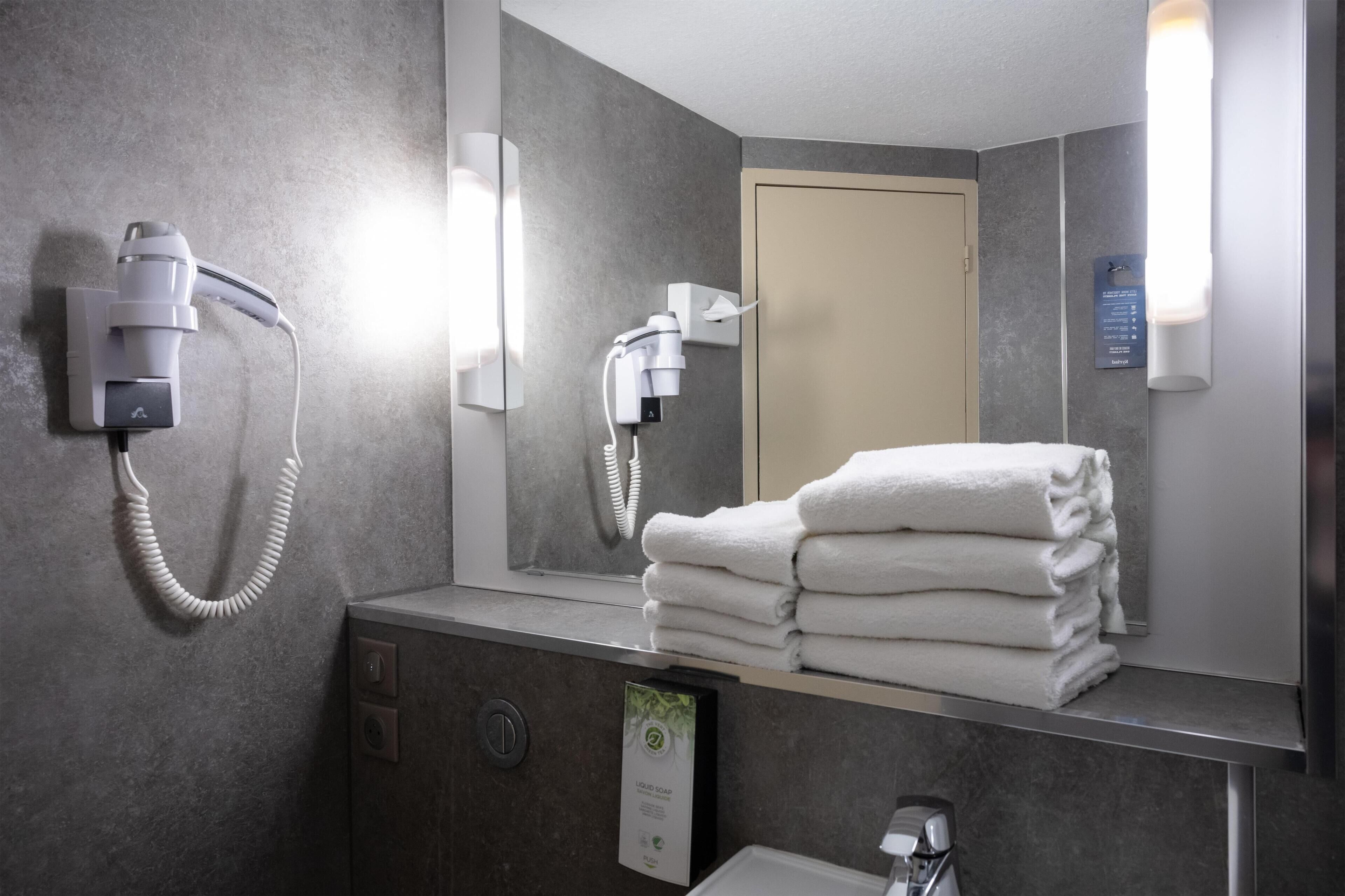 A bathroom with a hairdryer, a towel rack with folded towels, a mirror, and a wall-mounted sign.