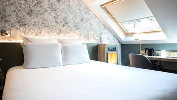 A bedroom with a skylight, a bed with white linens, a desk with a lamp, and a wall with a floral pattern.