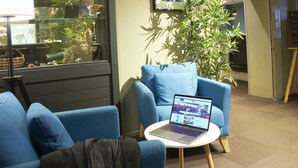 A modern waiting area with blue armchairs, a laptop on a small table, and a large potted plant. - Kyriad - Beaune (Beaune)
