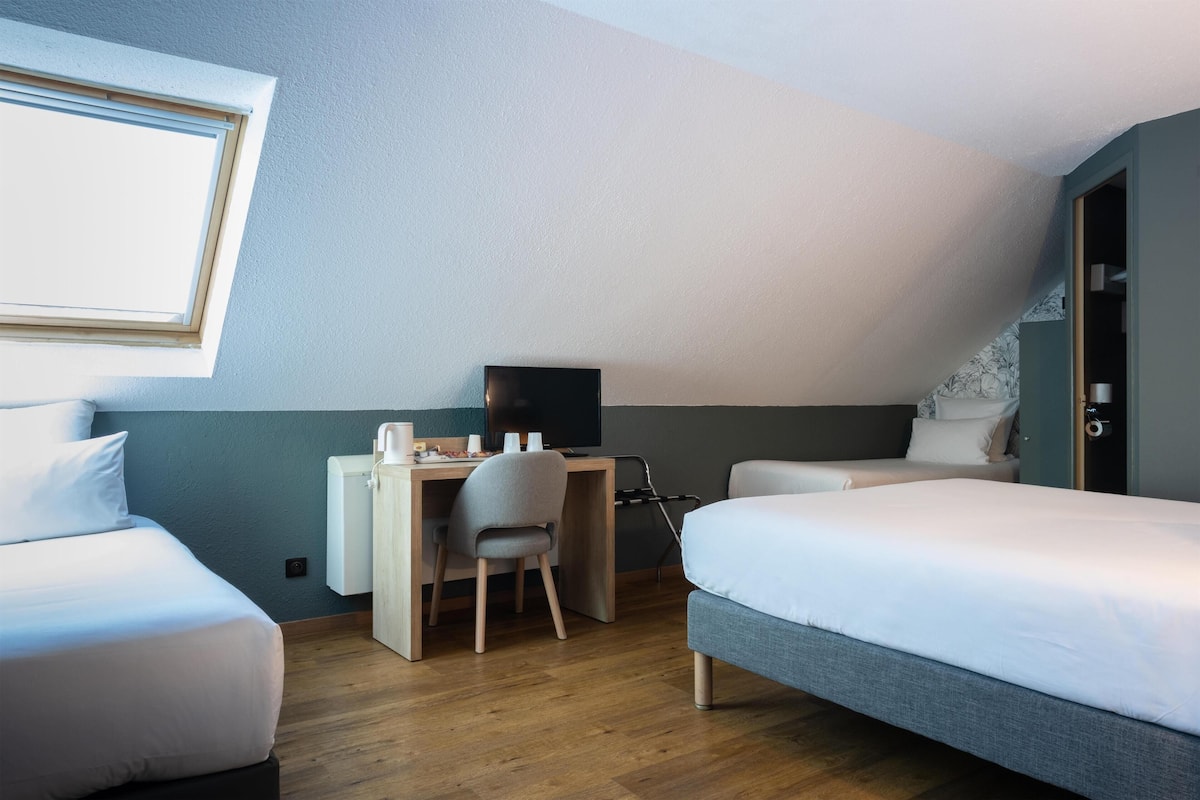 Une chambre avec deux lits, un bureau avec une chaise, une télévision et une fenêtre.