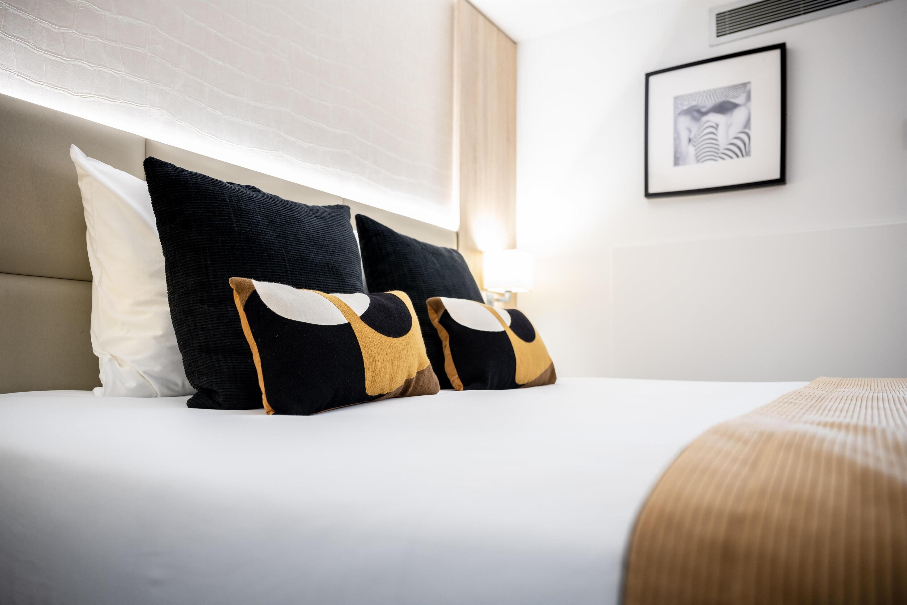 Una cama bien tendida con ropa blanca y tres almohadas decorativas.