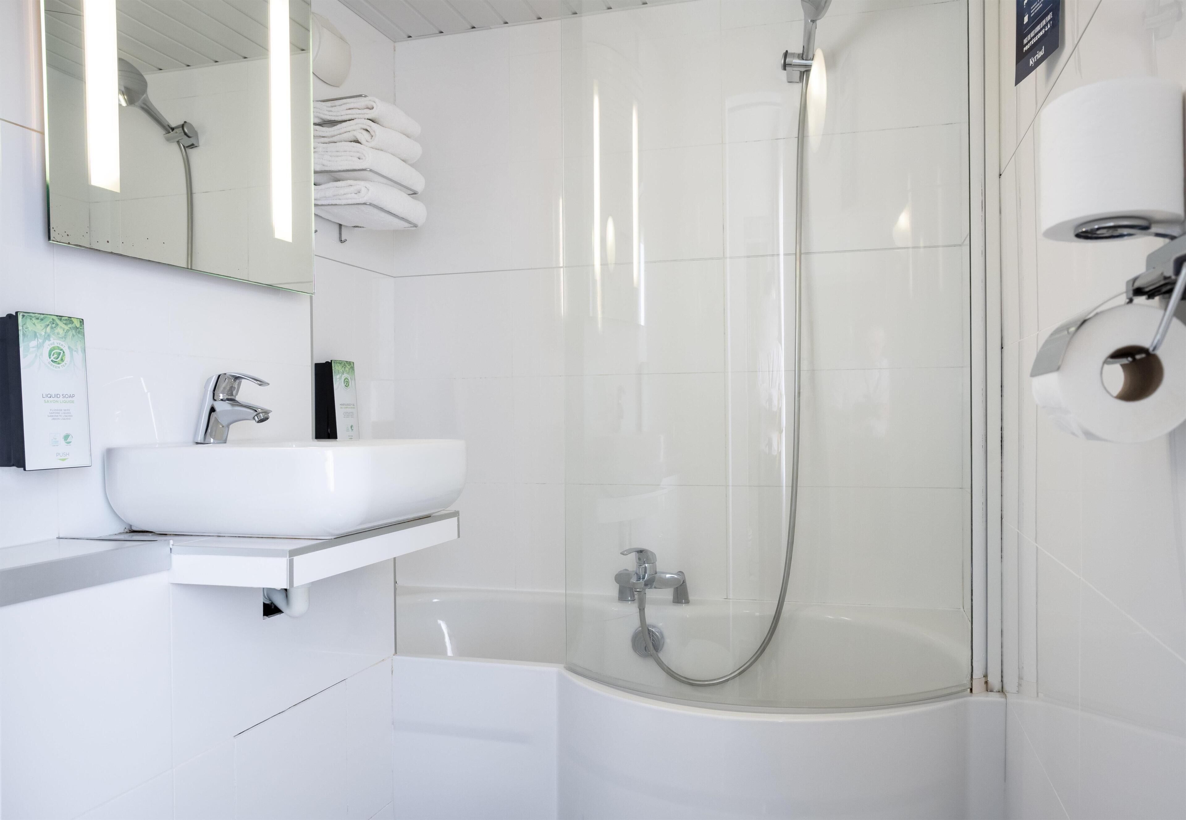 A modern bathroom with a white sink, mirror, and glass-enclosed shower.