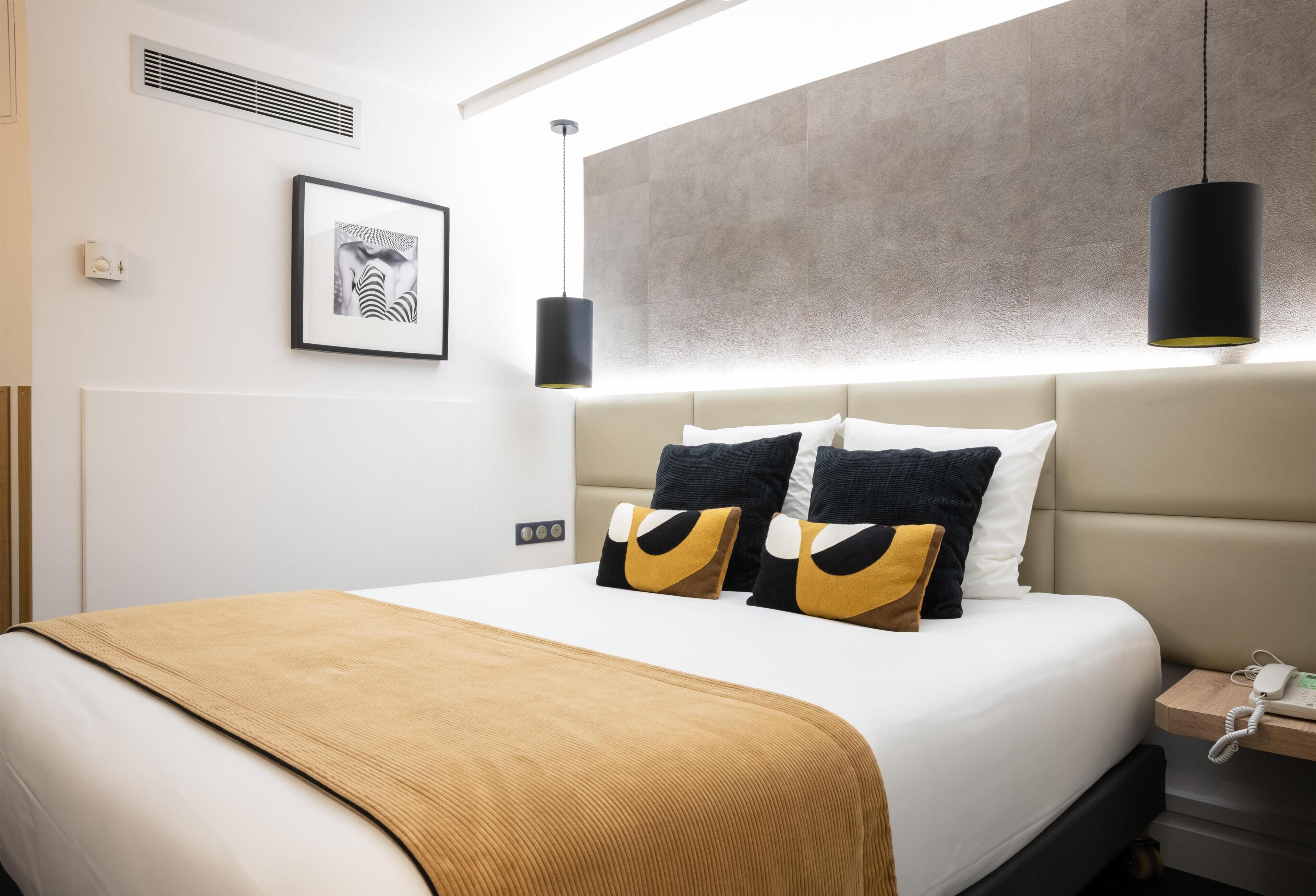 Una habitación de hotel moderna con una cama grande, un teléfono en la mesita de noche y un cuadro enmarcado en la pared.