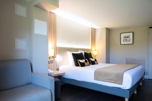 Una habitación de hotel con una cama, mesita de noche, lámpara y una silla.