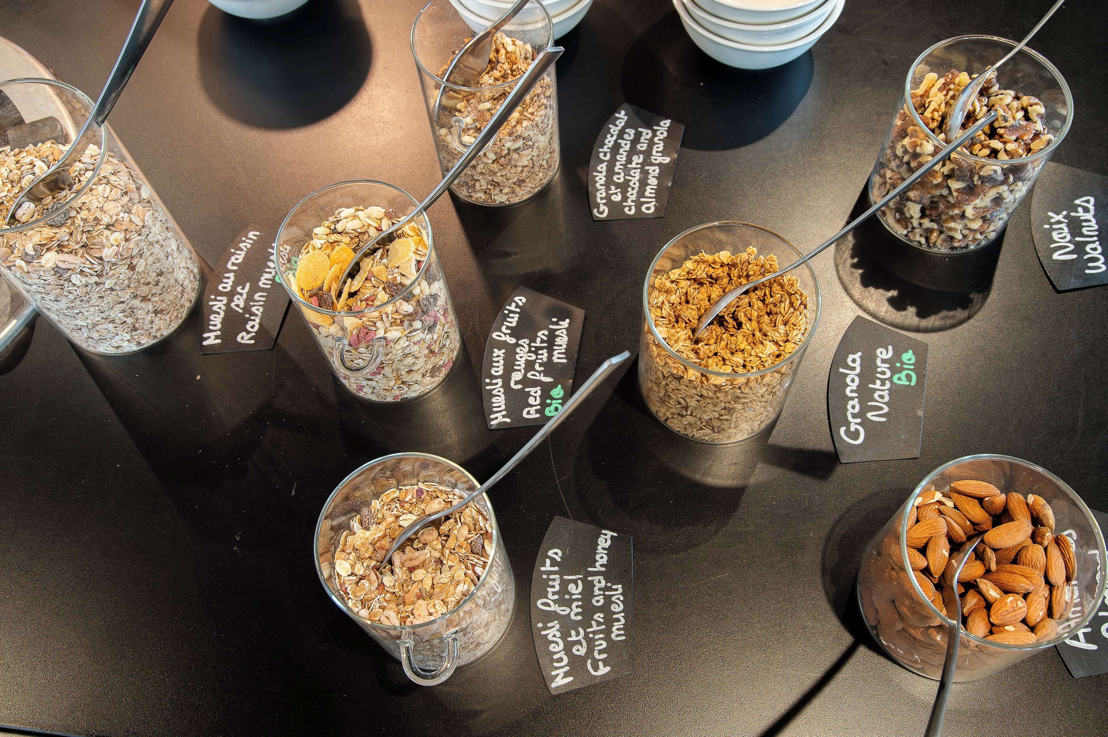 A variety of granola and nut mixes in clear containers with labels, arranged on a table.