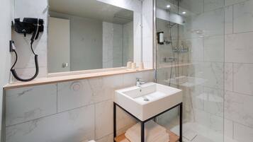 Un bagno moderno con doccia rivestita in marmo, un lavabo bianco su supporto in metallo nero e un asciugacapelli montato a parete.