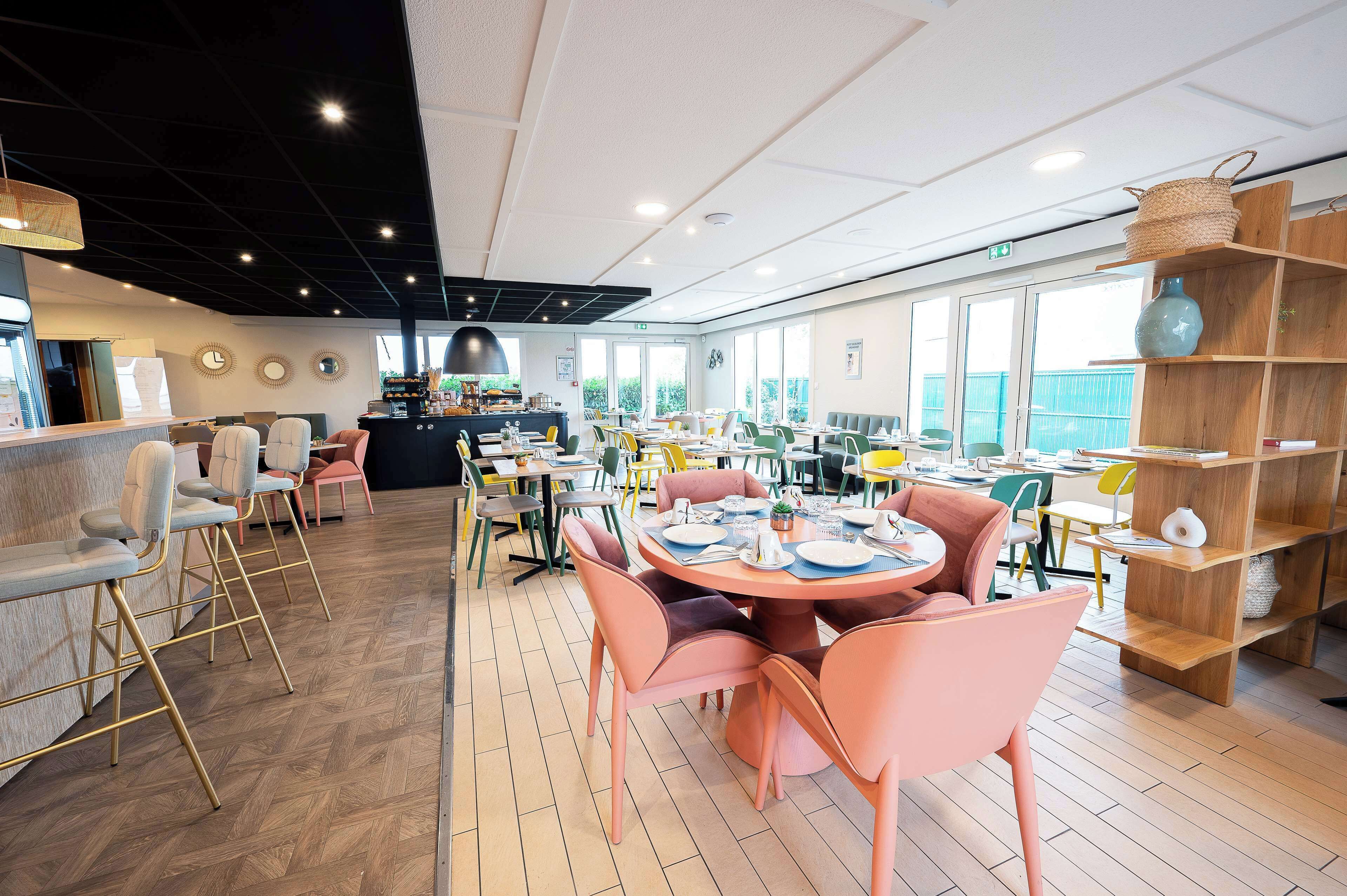 A modern dining area with round tables and chairs, a counter with a cash register, and large windows providing natural light.